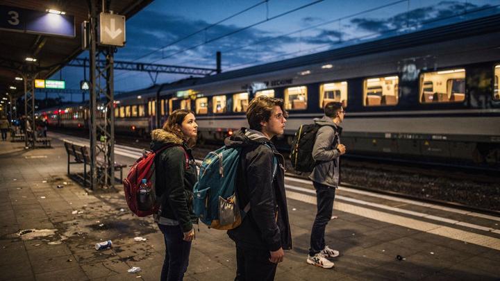 Students with backpacks waiting on a station platform next to a night train